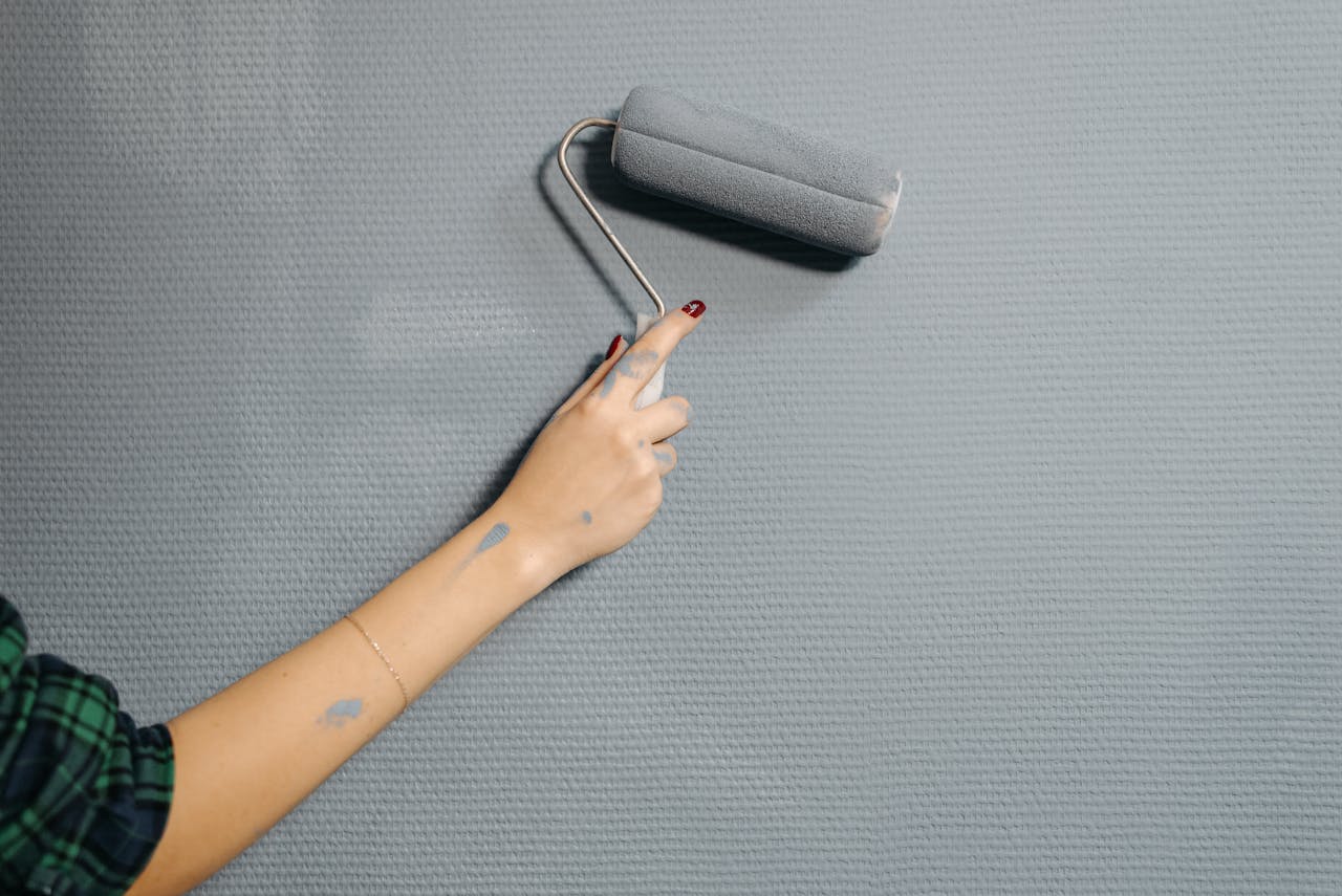 About A close-up of a persons hand using a paint roller on a blue wall for home renovation.